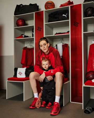 A mother and child in matching red Puma sneakers and apparel pose inside of a locker room with red and white lockers.