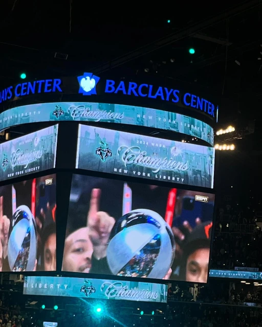 Interior view of Barclays Center screens displaying New York Liberty 'Champions' over a crowd, emphasizing sports and celebration.