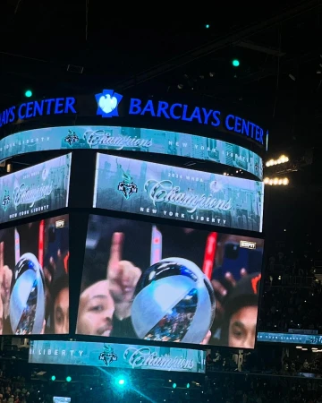 Interior view of Barclays Center screens displaying New York Liberty 'Champions' over a crowd, emphasizing sports and celebration.