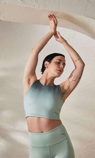 Athletic woman in sports bra and leggings with arms raised against a light-colored background for fitness and activewear.