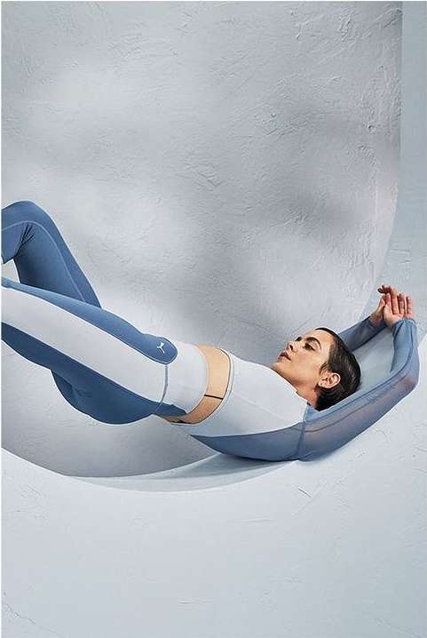 Athletic woman in activewear lies back in a studio with a geometric backdrop, showcasing fitness and fashion in a minimalist composition.