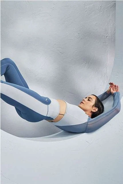 Athletic woman in activewear lies back in a studio with a geometric backdrop, showcasing fitness and fashion in a minimalist composition.