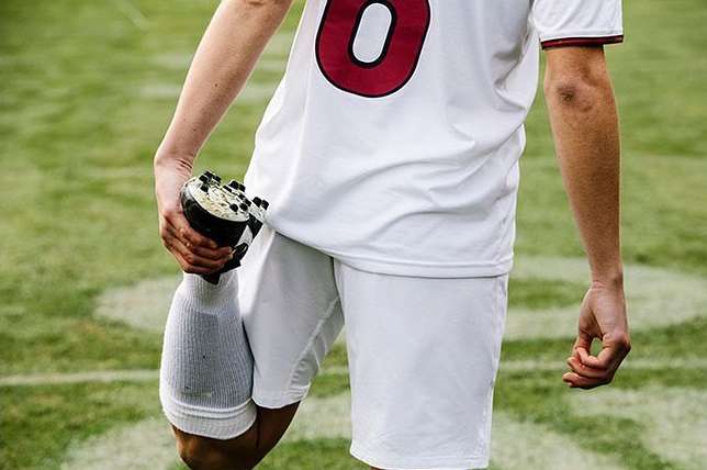 Athlete in uniform stretches leg on green field, preparing for a soccer game or sports event, showcasing fitness and athletic performance.