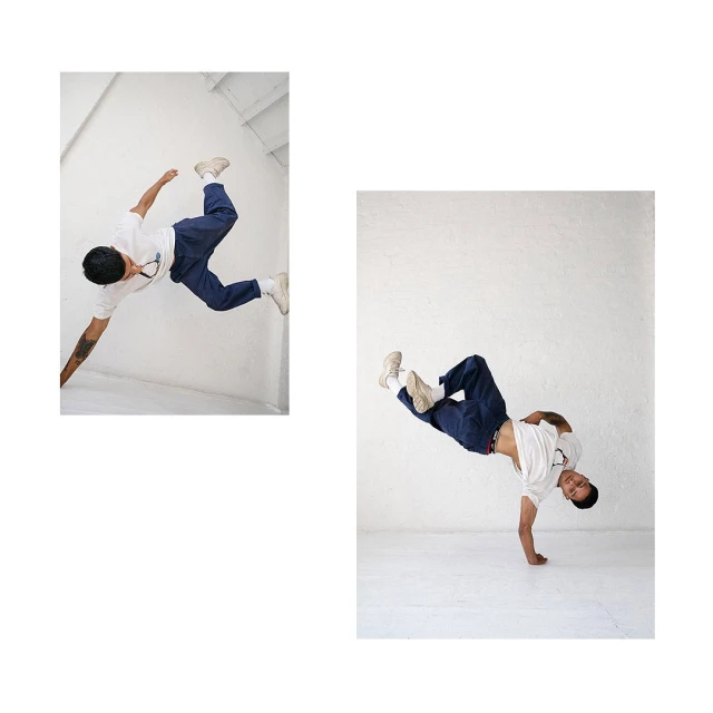Male dancer in mid-air pose, wearing a white shirt, and blue pants against a white background, showcasing acrobatic skill and athleticism.