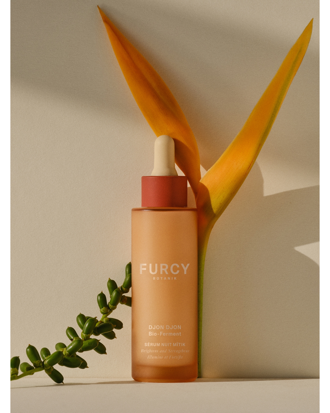 Furcy Botanics serum bottle with dropper, next to bird of paradise flower and leafy green branch. Minimalist product shot.