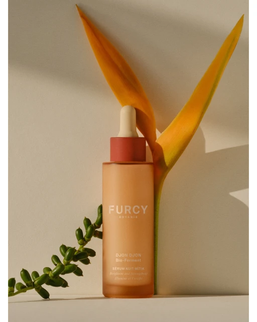 Furcy Botanics serum bottle with dropper, next to bird of paradise flower and leafy green branch. Minimalist product shot.