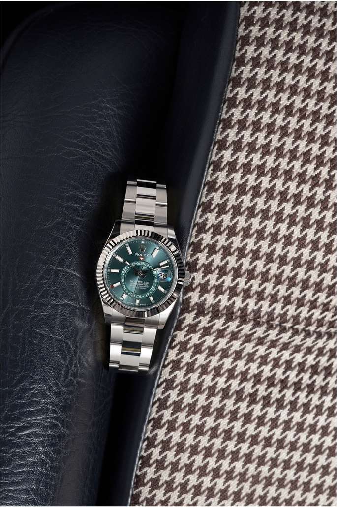 Wristwatch with silver band and green face displayed on a blue leather surface and a houndstooth patterned fabric background.