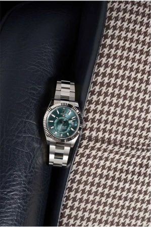 Wristwatch with silver band and green face displayed on a blue leather surface and a houndstooth patterned fabric background.