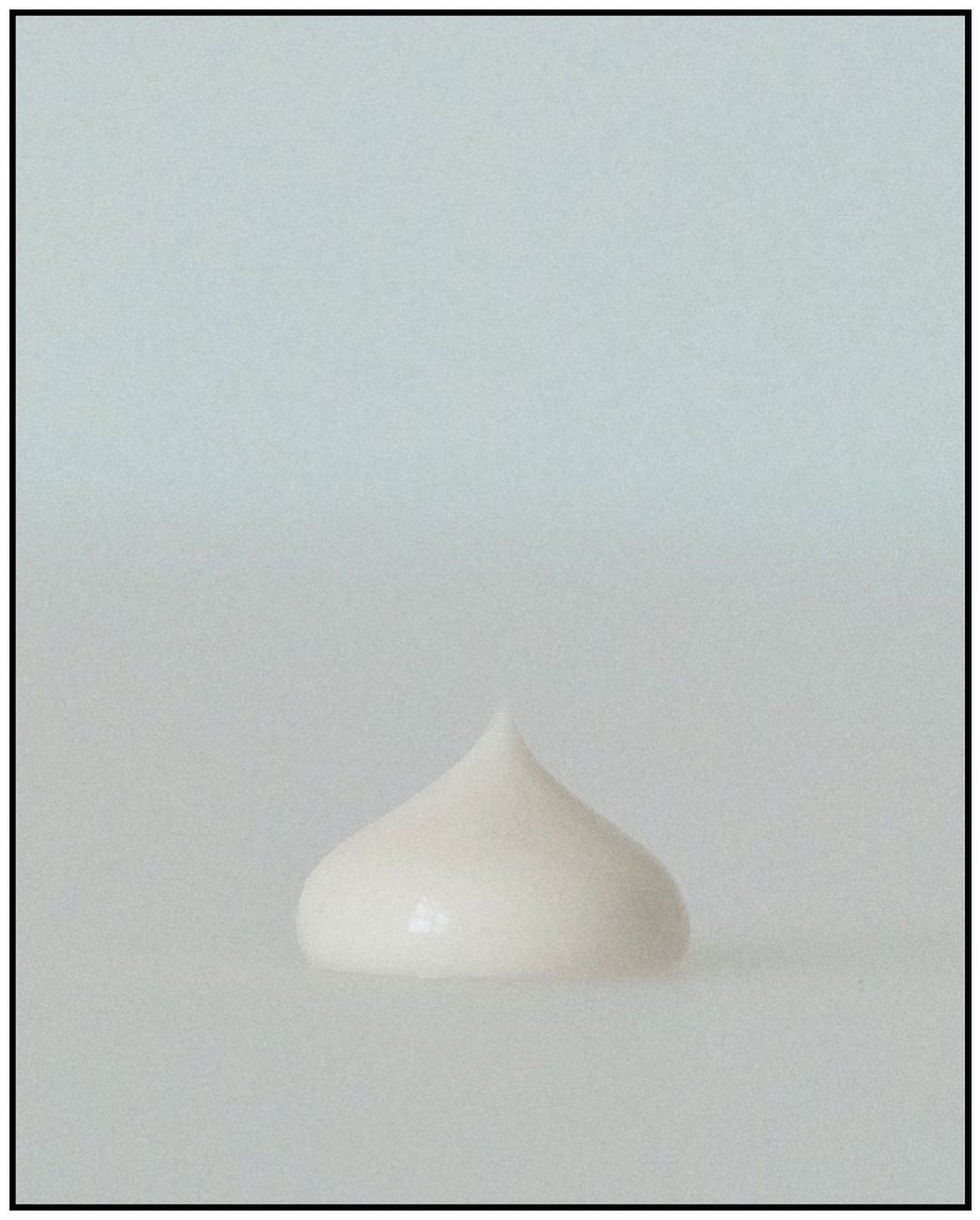 Close-up of a rounded peak of white cosmetic cream or lotion against a soft, diffused white background. Beauty product shot.