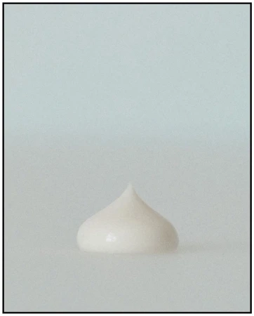 Close-up of a rounded peak of white cosmetic cream or lotion against a soft, diffused white background. Beauty product shot. 
