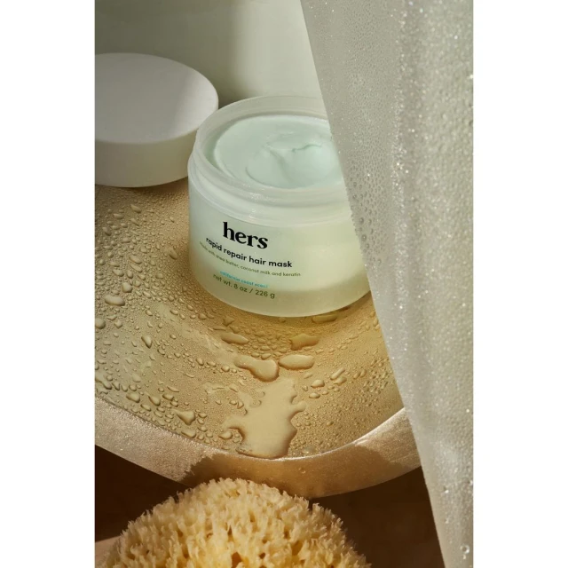 Close-up studio shot of hers rapid repair hair mask jar, complemented by a white lid and a natural sponge, set against a neutral backdrop.