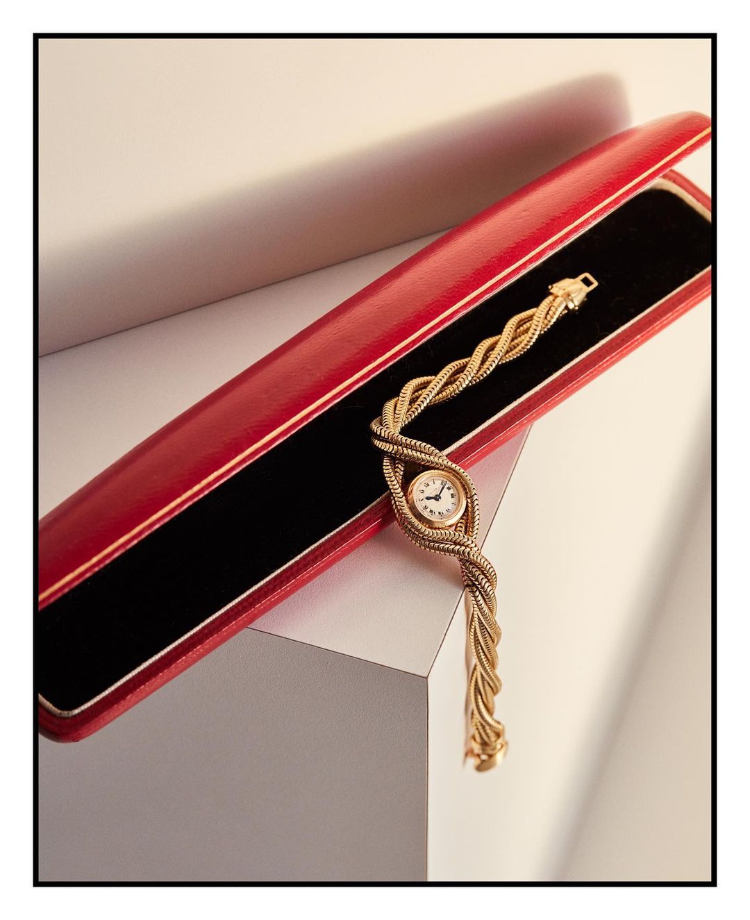 Close-up of a gold woven wristwatch in a red presentation box against a neutral backdrop, showcasing luxury watch design and detail.