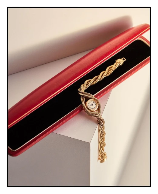 Close-up of a gold woven wristwatch in a red presentation box against a neutral backdrop, showcasing luxury watch design and detail.