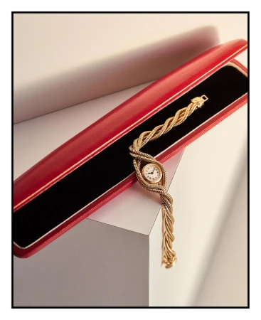 Close-up of a gold woven wristwatch in a red presentation box against a neutral backdrop, showcasing luxury watch design and detail.