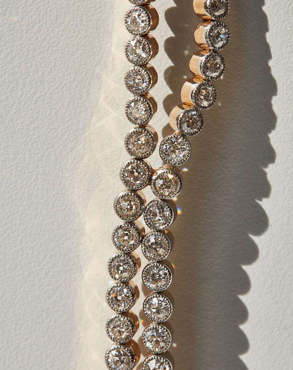 Close-up of a two-strand diamond tennis bracelet with gold setting. Diamonds are clear and brilliant, reflecting the light. Background is white.