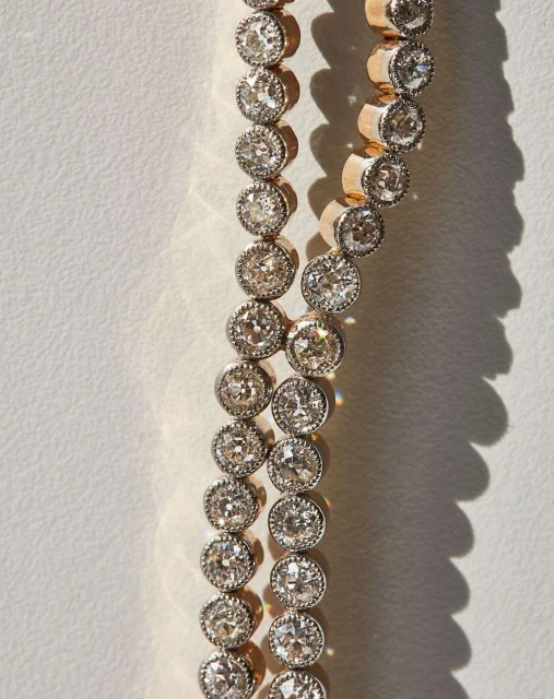 Close-up of a two-strand diamond tennis bracelet with gold setting. Diamonds are clear and brilliant, reflecting the light. Background is white.