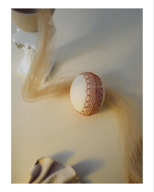 Artful still life featuring an ornamented egg, flowing blonde hair, and sculptural elements, all bathed in soft, diffused studio lighting.