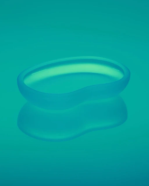 Translucent blue glass dish with a smooth, curved design on a matching reflective blue background. Minimalist studio product shot.