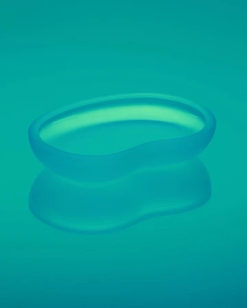 Translucent blue glass dish with a smooth, curved design on a matching reflective blue background. Minimalist studio product shot.