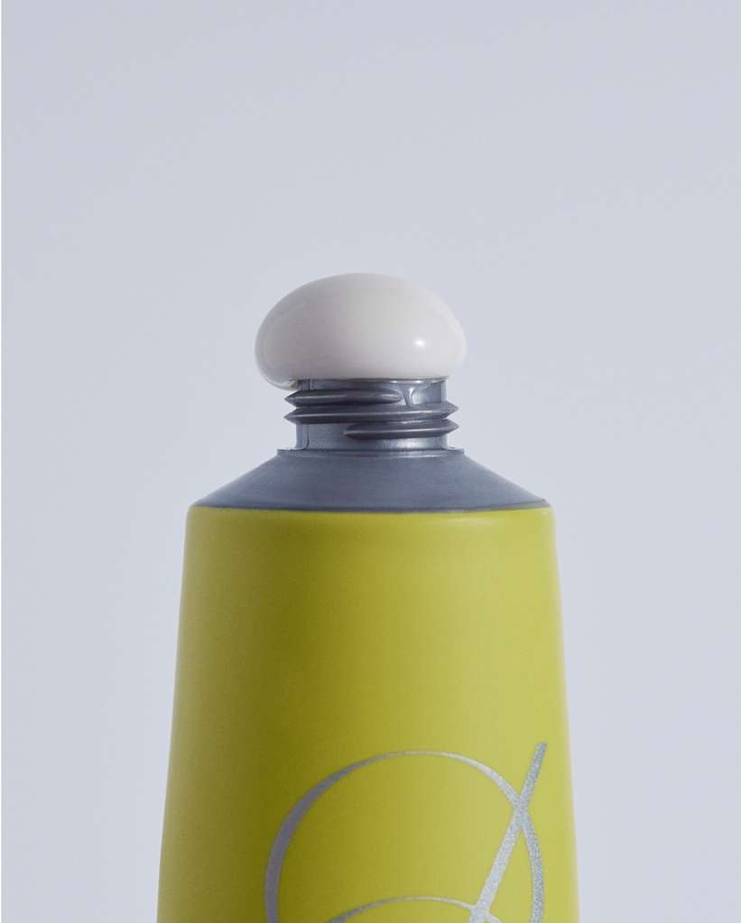 Close-up of a green and gray cosmetic tube with a round, off-white cap against a plain white background, showcasing product details.