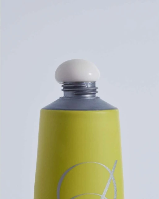 Close-up of a green and gray cosmetic tube with a round, off-white cap against a plain white background, showcasing product details.