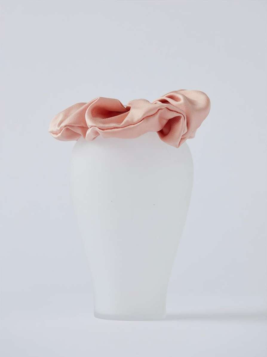 Close-up of a satin scrunchie in light pink on a mannequin head against a neutral background, showcasing texture and color for fashion.