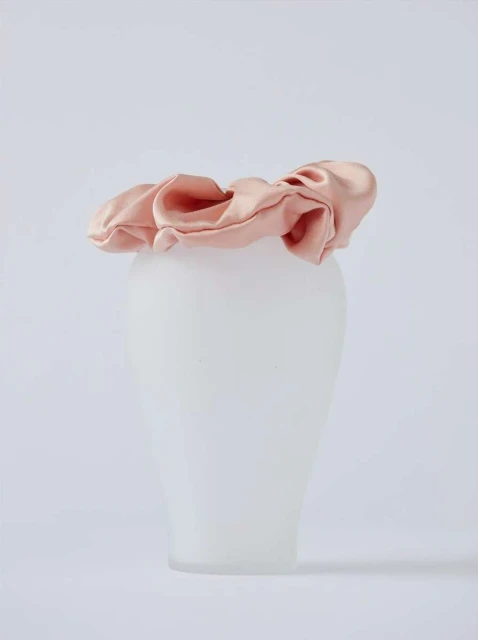 Close-up of a satin scrunchie in light pink on a mannequin head against a neutral background, showcasing texture and color for fashion.