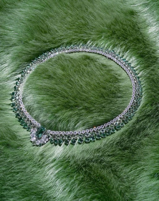 Diamond and emerald necklace displayed on a light green fur surface, showcasing fine jewelry and luxurious materials.