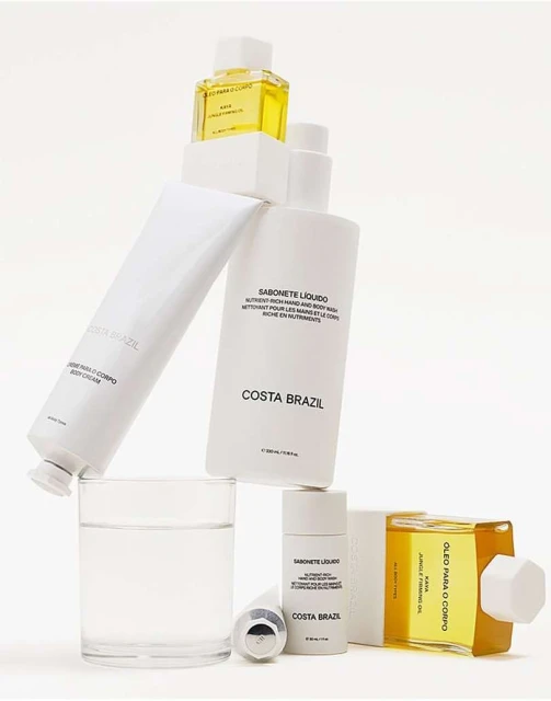 Costa Brazil skincare product line displayed in a minimal white setting, featuring body cream, liquid soap, and body oil.