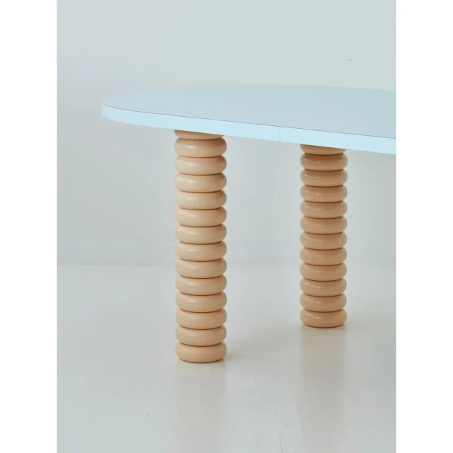 Close-up of a contemporary blue table with unique cylindrical wooden legs in a minimalist interior setting, showcasing modern furniture design.