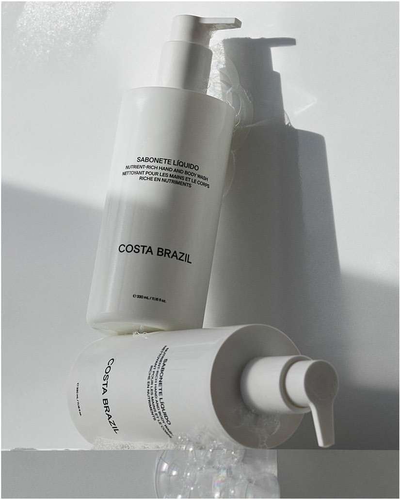 Costa Brazil liquid soap bottles in a minimalist product shot with soft shadows and bubbles on a white surface; beauty product promotion.