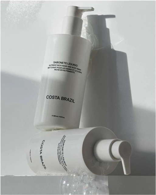 Costa Brazil liquid soap bottles in a minimalist product shot with soft shadows and bubbles on a white surface; beauty product promotion.