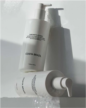 Costa Brazil liquid soap bottles in a minimalist product shot with soft shadows and bubbles on a white surface; beauty product promotion.