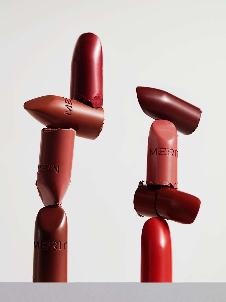 Stacked arrangement of Merit brand lipsticks in various shades against a white background, beauty and cosmetic product photography.