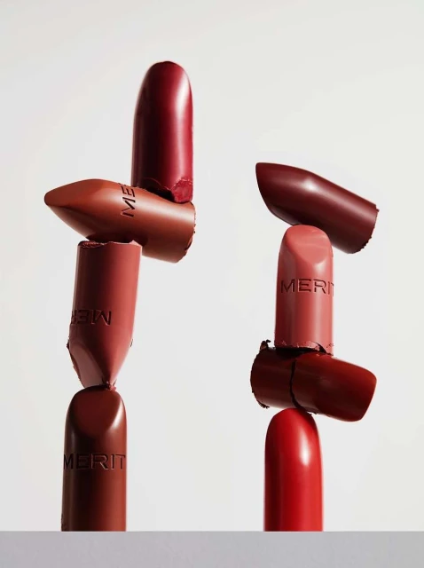 Stacked arrangement of Merit brand lipsticks in various shades against a white background, beauty and cosmetic product photography.