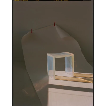 Minimalist still life photograph of a translucent acrylic stool casting long shadows on a white backdrop with visible film border.