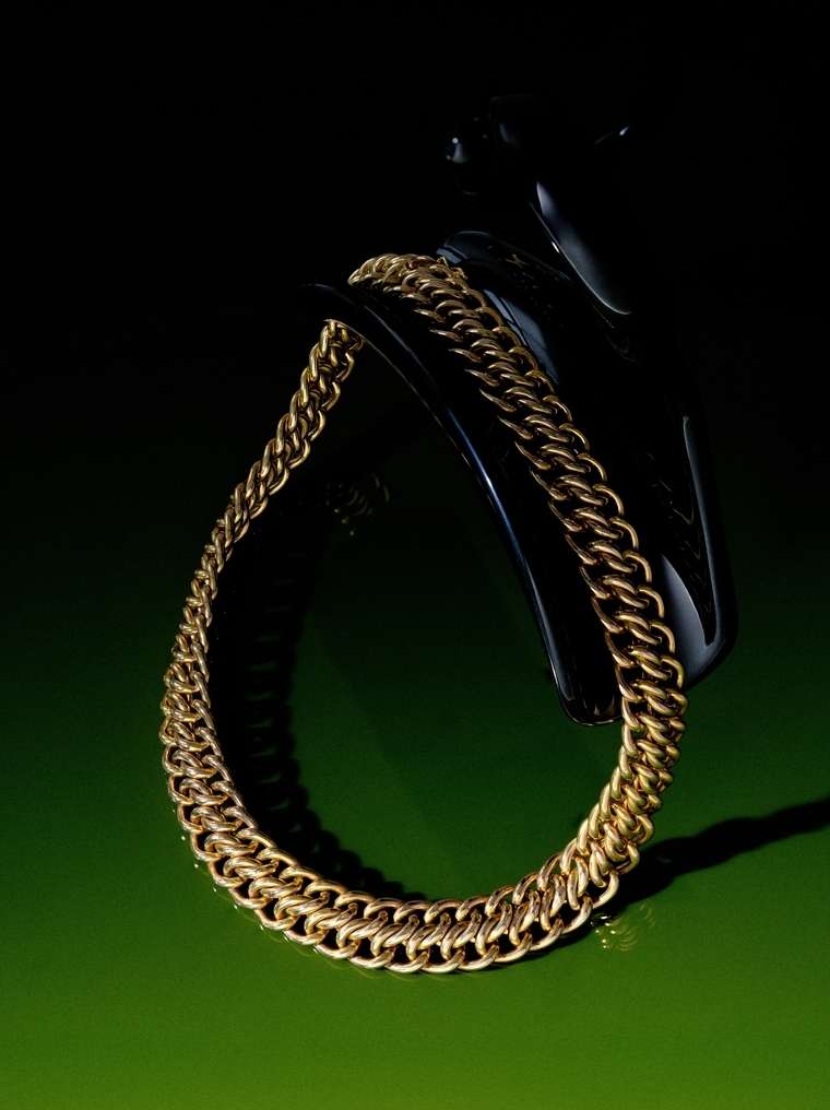 Gold chain necklace sits atop a black display stand on a green surface, creating a striking contrast in a dimly lit setting.