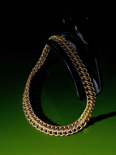 Gold chain necklace sits atop a black display stand on a green surface, creating a striking contrast in a dimly lit setting.