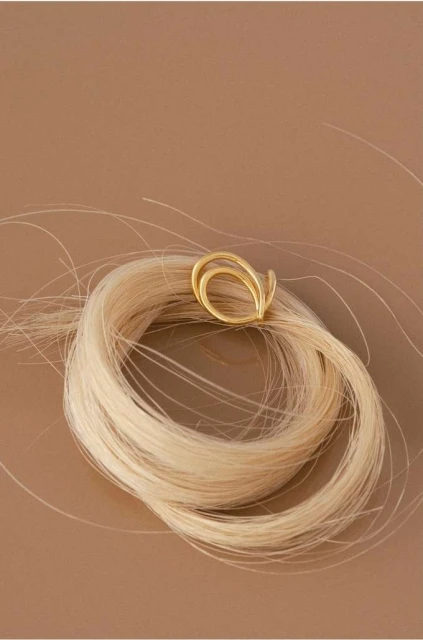 Close-up of a gold ring placed on a swirl of blond hair against a tan background. Jewelry shot for beauty or fashion.