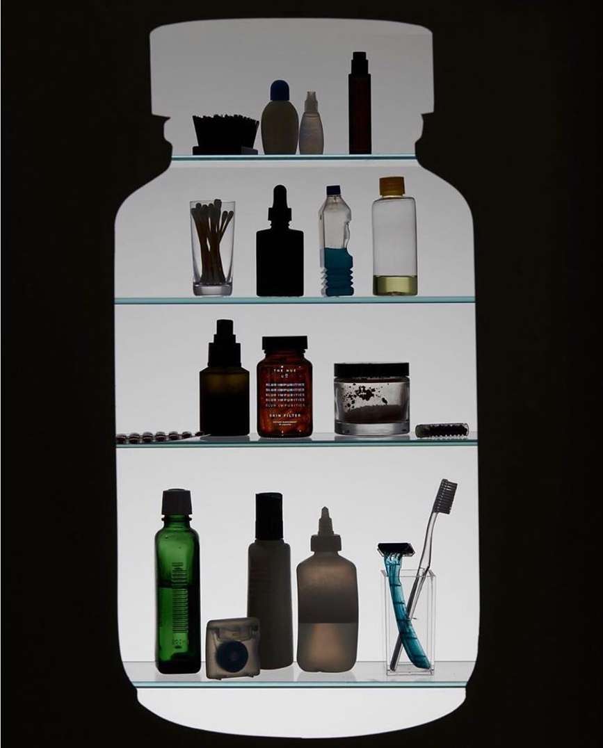 Illuminated bathroom cabinet containing toiletries such as bottles, dental floss, cotton swabs, shaving razor, and toothbrush in a dark setting.