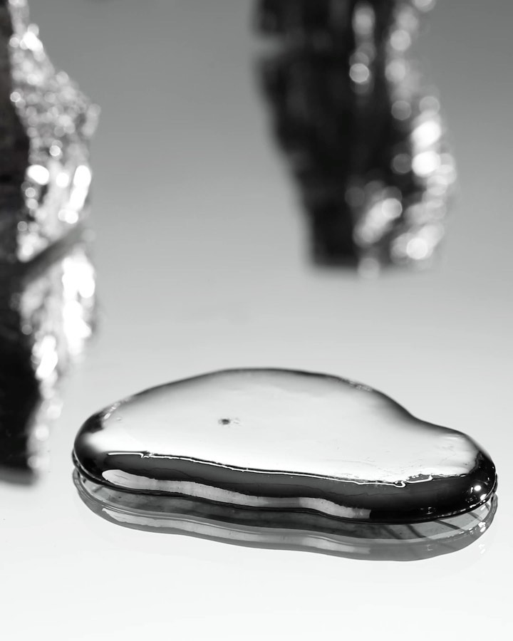 Macro photograph of a droplet of liquid mercury. Metal substance reflects light on a white surface. Silver colored fluid.