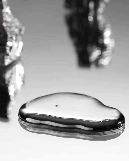 Macro photograph of a droplet of liquid mercury. Metal substance reflects light on a white surface. Silver colored fluid.