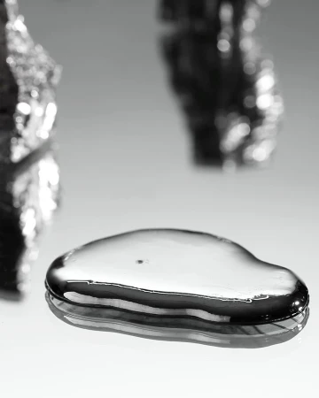 Macro photograph of a droplet of liquid mercury. Metal substance reflects light on a white surface. Silver colored fluid.
