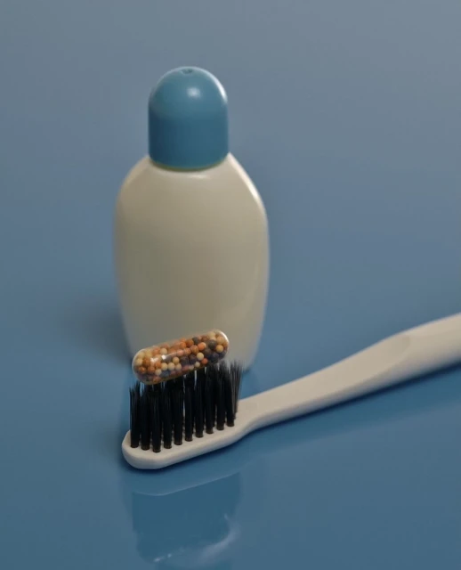 Toothbrush with black bristles, clear capsule filled with tiny colorful beads on top, white and blue bottle on a blue backdrop.