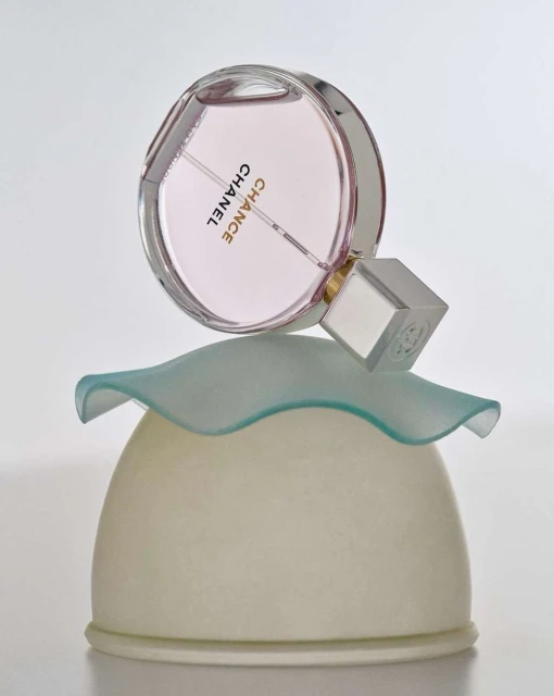 Elegant still life featuring a Chanel Chance perfume bottle on a sculpted ivory-and-aqua glass stand against a soft white backdrop.