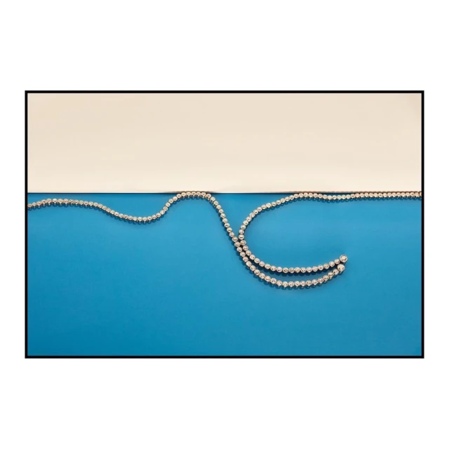 Necklace with white gemstones in sinuous arrangement against a blue and white background; jewellery photography.