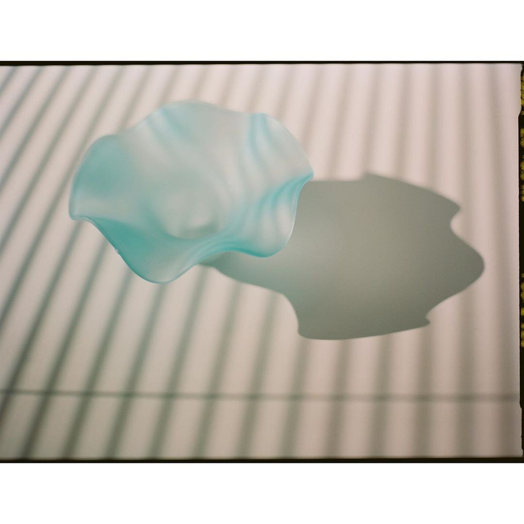 Abstract photograph of a translucent teal glass dish casting shadows against a neutral background with linear shadow pattern.