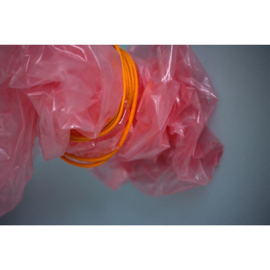 Close-up of orange rope-like cables in a stack, inside a pink plastic bag, against a light blue background, showcasing texture and color.