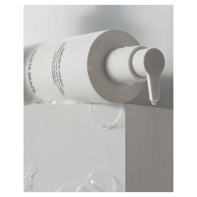 Costa Brazil Sabonete Liquido soap dispenser with water droplets, minimalist product shot, pristine white and modern presentation.