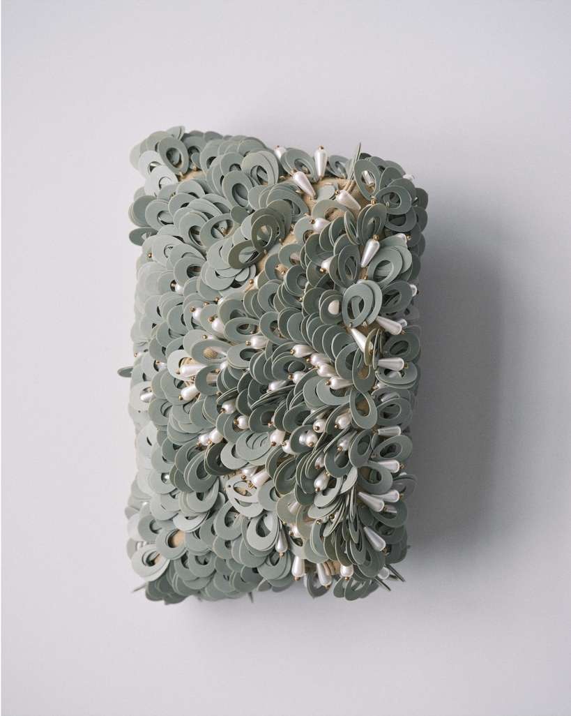 Abstract wall art featuring circular paper discs and droplet-shaped beads, creating a textured and unique decorative piece on white wall.